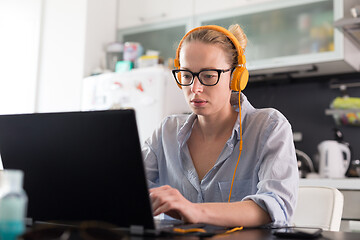 Image showing Female freelancer in her casual home clothing working remotly from her dining table in the morning. Home kitchen in the background.