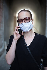 Image showing COVID-19 pandemic coronavirus. Casual caucasian woman at medieval city street using mobile phone, wearing protective face mask against spreading of coronavirus and disease transmission