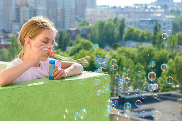 Image showing Girl blows hearty soap bubbles from the balcony of a high-rise building