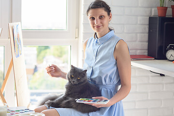 Image showing Girl draws with brushes and watercolors on an easel, a cat sits on her lap