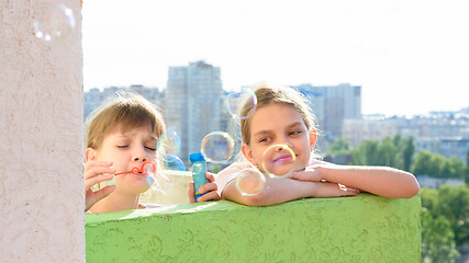 Image showing Girl watching her sister blow bubbles on the balcony of the house