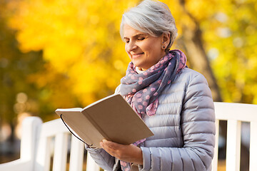 Image showing happy senior woman reading diary at autumn park