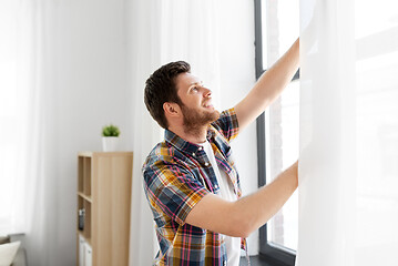 Image showing young man opening window curtain at home