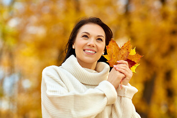 Image showing happy young woman with maple leaves in autumn park