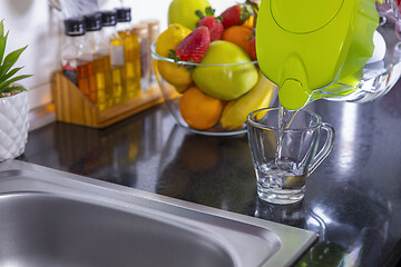 Image showing Pouring filtered water into glass from jug in the kitchen