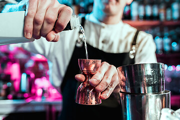 Image showing Expert barman is making cocktail at night club.