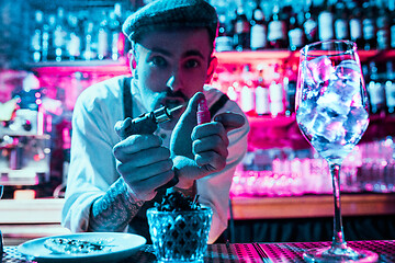 Image showing Expert barman is making cocktail at night club.