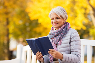 Image showing happy senior woman reading book at autumn park