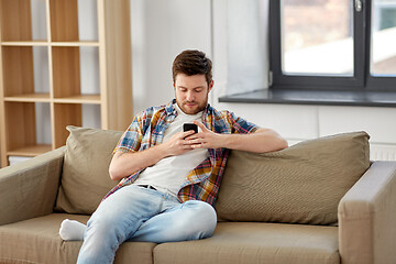 Image showing man with smartphone sitting on sofa at new home