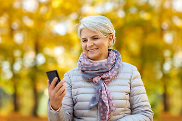 Image showing happy senior woman with smartphone at autumn park