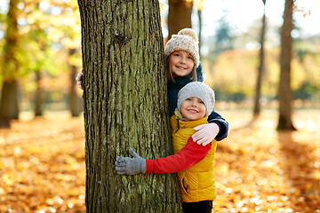 Image showing happy children peeking out tree at autumn park