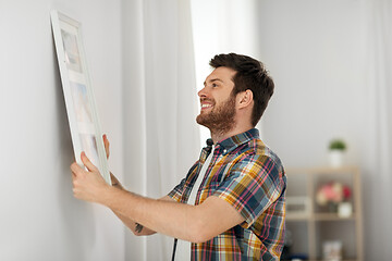 Image showing man hanging picture in frame to wall at home