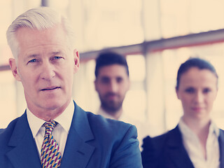 Image showing portrait of senior businessman as leader  with staff in backgrou