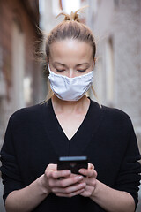 Image showing COVID-19 pandemic coronavirus. Casual caucasian woman at medieval city street using mobile phone, wearing protective face mask against spreading of coronavirus and disease transmission