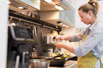 Image showing Stay at home housewife woman cooking in kitchen, salting dish in a saucepan, preparing food for family dinner.