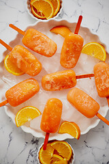 Image showing Homemade, juicy, orange popsicles. Placed on a white plate with ice cubes