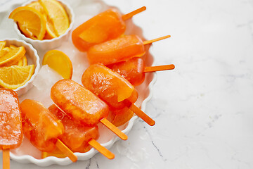 Image showing Homemade, juicy, orange popsicles. Placed on a white plate with ice cubes