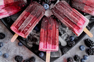 Image showing Homemade fresh frozen blueberry and blackberry popsicles on black plate with ice sitting on stone