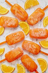 Image showing Homemade frozen popsicles made with oragnic fresh oranges placed with ice cubes on marble table