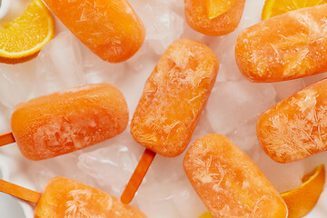 Image showing Homemade frozen popsicles made with oragnic fresh oranges placed with ice cubes on marble table