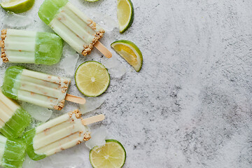 Image showing Lime and cream homemade popsicles or ice creams placed with ice cubes on gray stone backdrop