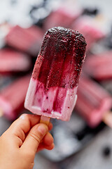 Image showing Close up on kid\'s hand holding colorful blueberry fruit popsicle. Healthy summer snack concept.