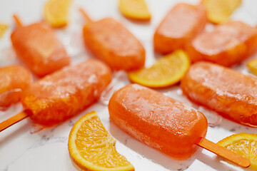 Image showing Homemade frozen popsicles made with oragnic fresh oranges placed with ice cubes on marble table