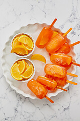 Image showing Homemade, juicy, orange popsicles. Placed on a white plate with ice cubes