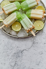 Image showing Lime and cream homemade popsicles or ice creams placed with ice cubes on gray stone backdrop