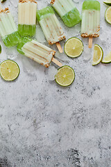 Image showing Lime and cream homemade popsicles or ice creams placed with ice cubes on gray stone backdrop