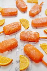 Image showing Homemade frozen popsicles made with oragnic fresh oranges placed with ice cubes on marble table