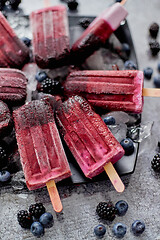 Image showing Homemade fresh frozen blueberry and blackberry popsicles on black plate with ice sitting on stone