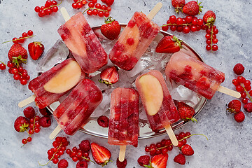 Image showing Homemade raspberry, strawberry, apple and currant popsicles on metal plate with ice assorted berries