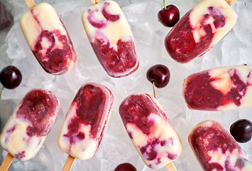 Image showing Homemade, delicious, cherry and milk ice cream popsicles placed on glass tray filled with ice cubes