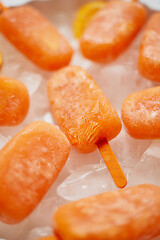 Image showing Homemade frozen popsicles made with oragnic fresh oranges placed with ice cubes on marble table