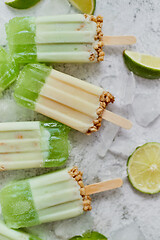 Image showing Lime and cream homemade popsicles or ice creams placed with ice cubes on gray stone backdrop