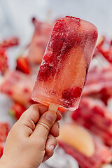 Image showing Close up on kid\'s hand holding colorful red berry fruit popsicle. Healthy summer snack concept.