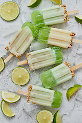 Image showing Lime and cream homemade popsicles or ice creams placed with ice cubes on gray stone backdrop