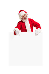 Image showing Happy Santa Claus pointing on blank advertisement banner background with copy space. Smiling Santa Claus pointing in white blank sign