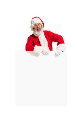 Image showing Happy Santa Claus pointing on blank advertisement banner background with copy space. Smiling Santa Claus pointing in white blank sign