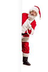 Image showing Happy Santa Claus pointing on blank advertisement banner background with copy space. Smiling Santa Claus pointing in white blank sign