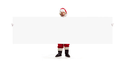 Image showing Happy Santa Claus pointing on blank advertisement banner background with copy space. Smiling Santa Claus pointing in white blank sign