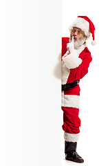 Image showing Happy Santa Claus pointing on blank advertisement banner background with copy space. Smiling Santa Claus pointing in white blank sign