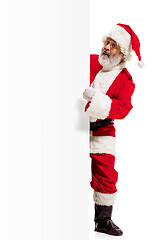 Image showing Happy Santa Claus pointing on blank advertisement banner background with copy space. Smiling Santa Claus pointing in white blank sign