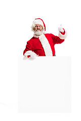 Image showing Happy Santa Claus pointing on blank advertisement banner background with copy space. Smiling Santa Claus pointing in white blank sign