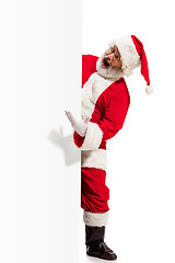 Image showing Happy Santa Claus pointing on blank advertisement banner background with copy space. Smiling Santa Claus pointing in white blank sign