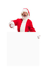 Image showing Happy Santa Claus pointing on blank advertisement banner background with copy space. Smiling Santa Claus pointing in white blank sign