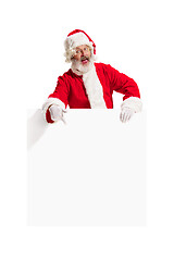 Image showing Happy Santa Claus pointing on blank advertisement banner background with copy space. Smiling Santa Claus pointing in white blank sign