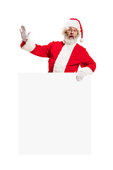 Image showing Happy Santa Claus pointing on blank advertisement banner background with copy space. Smiling Santa Claus pointing in white blank sign