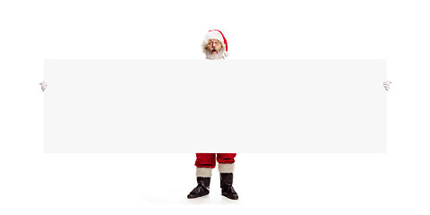 Image showing Happy Santa Claus pointing on blank advertisement banner background with copy space. Smiling Santa Claus pointing in white blank sign